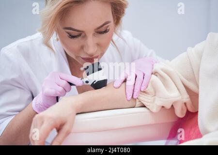Medico attento che controlla la pelle del paziente con dermatoscopio Foto Stock
