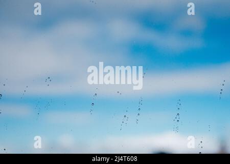 Pioggia su una finestra contro il cielo blu con le nuvole Foto Stock