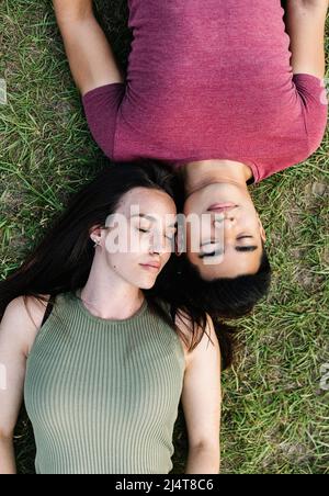 Vista dall'alto della giovane coppia con occhi chiusi che si stendano sull'erba del parco pubblico Foto Stock