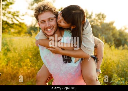 Coppia giovane multirazziale baciare e piggybacking all'aperto Foto Stock