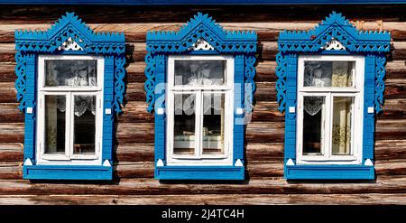 Vecchie finestre in legno con architravi intagliati. Facciata in legno di tipica casa rurale russa. Foto Stock