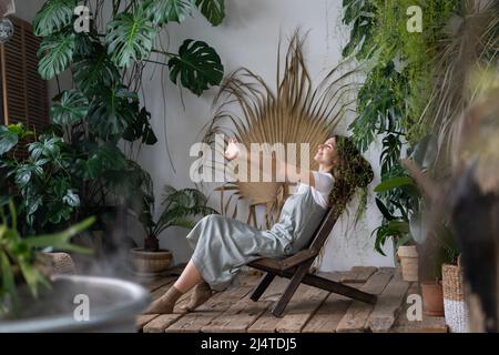 Soddisfatto calmo donna fiorista rilassarsi in giardino interno godere di equilibrio mentale e benessere a casa Foto Stock