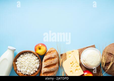 Felice concetto Shavuot. Cornice fatta di pane di cereali, formaggio casereccio, bottiglia di latte, grano, formaggio su sfondo blu. Saluto di festa religiosa ebraica Foto Stock