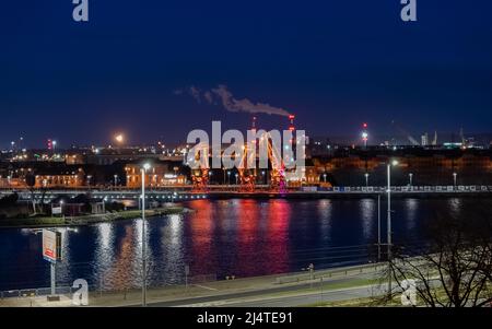 I tre vecchi porti si gru dall'isola di Szczecin di Lasztownia colorfully illuminato. Città di notte. Polonia. Dalla distanza che assomiglia ai dinosauri. P Foto Stock