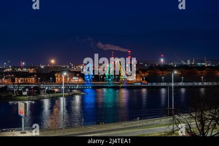 I tre vecchi porti si gru dall'isola di Szczecin di Lasztownia colorfully illuminato. Città di notte. Polonia. Dalla distanza che assomiglia ai dinosauri. P Foto Stock