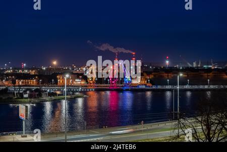 I tre vecchi porti si gru dall'isola di Szczecin di Lasztownia colorfully illuminato. Città di notte. Polonia. Dalla distanza che assomiglia ai dinosauri. P Foto Stock