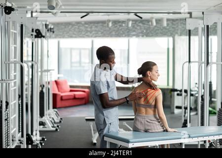 Riabilitazione terapista mettere cinesio nastro sulla schiena e spalla della giovane donna in clinica di fisioterapia, copia spazio Foto Stock