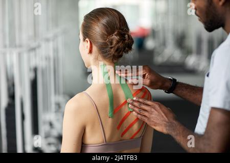 Primo piano di terapista mettere cinesio nastro sulla schiena e spalla della giovane donna in fisioterapia sessione Foto Stock