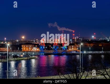 I tre vecchi porti si gru dall'isola di Szczecin di Lasztownia colorfully illuminato. Città di notte. Polonia. Dalla distanza che assomiglia ai dinosauri. P Foto Stock