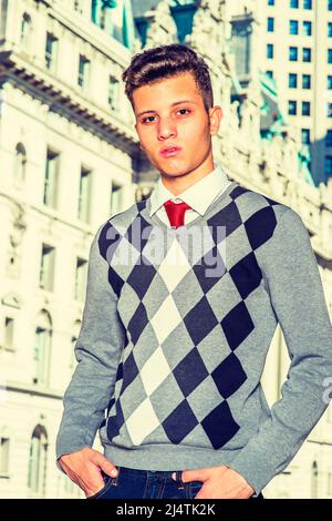 Ritratto di studente universitario. Vestirsi in un maglione nero, bianco, grigio, jeans, mani in tasche, un giovane uomo d'affari bello sta in piedi dentro Foto Stock