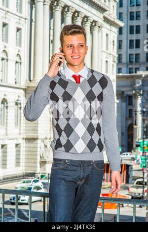 Uomo che chiama all'esterno. Vestendo in un nero, bianco, grigio, pullover a motivi geometrici, jeans, un giovane uomo d'affari bello è in piedi davanti ad un bui ufficio Foto Stock