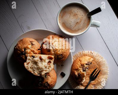 Muffin con scaglie di cioccolato su un piatto bianco con una tazza di caffè bianco sullo sfondo. Foto Stock