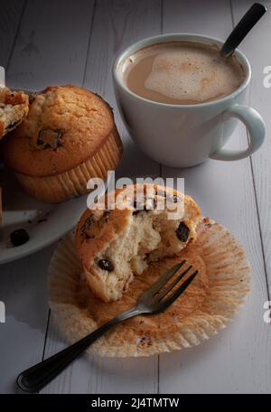 Muffin con scaglie di cioccolato su un piatto bianco con una tazza di caffè bianco sullo sfondo. Foto Stock
