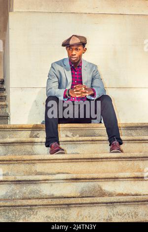 Uomo Urbano Moda. Indossare un cappello Apple Newsboy, vestirsi in blazer grigio chiaro, rosa a motivi geometrici, nero sotto la camicia, pantaloni neri, scarpe in pelle marrone, r Foto Stock