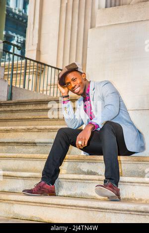 Uomo Urbano Moda. Indossare un cappello Apple Newsboy, vestirsi in blazer grigio chiaro, rosa a motivi geometrici, nero sotto la camicia, pantaloni neri, scarpe in pelle marrone, r Foto Stock