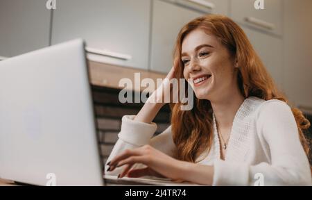 Donna incavata che lavora e digita sulla tastiera a casa utilizzando la tecnologia del computer portatile mentre si siede sul tavolo. Ritratto di donna d'affari. Casa intelligente Foto Stock