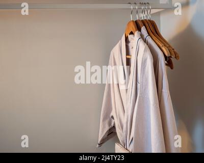 Coppia di accappatoi in cotone in stile giapponese appesi sugli appendiabiti in legno sul rack all'interno del guardaroba bianco per gli ospiti dell'hotel nelle luci soffuse wi Foto Stock