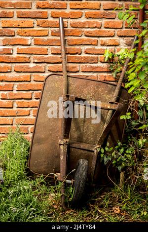 vecchia carriola appoggiata al muro di mattoni Foto Stock