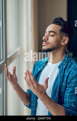 Un giovane barbuto che prega con gli occhi chiusi Foto Stock