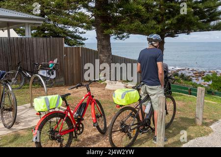 Maschio di mezza età o anziano a cavallo di una bicicletta elettrica che guarda verso l'oceano, Avalon Beach, Sydney, Australia Foto Stock