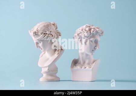 Due piccoli busti di giovani uomini romani o greci di stile antico che si affacciano l'uno dall'altro sul blu Foto Stock