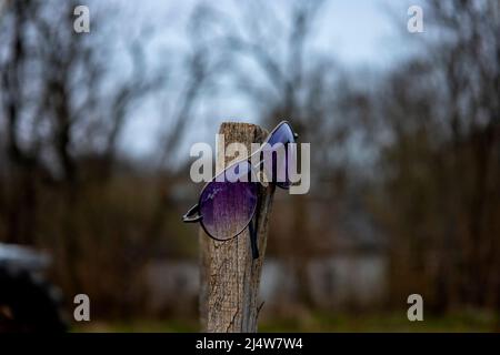 Occhiali da sole su un palo di legno. Sfondo sfocato. Foto Stock