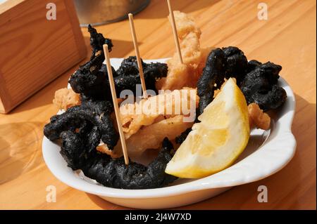 Tradizionale calamari croccanti in stile spagnolo, alcuni fritti con inchiostro di calamari e serviti con un cuneo di limone Foto Stock