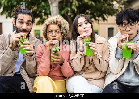 Gruppo di giovani amici multirazziali che fanno volti divertenti mentre bevono all'aperto Foto Stock