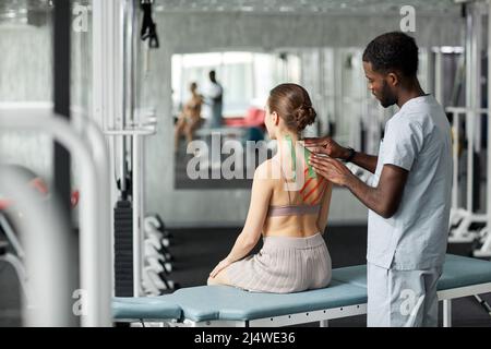 Riabilitazione terapista mettere cinesio nastro sulla schiena e spalla della giovane donna in fisioterapia sessione Foto Stock