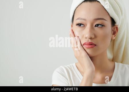 Giovane donna che soffre di mal di denti, tocca la guancia e guarda via Foto Stock