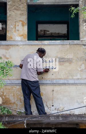 Uomo che dipinge un segno non per la vendita sulla facciata di una casa dilapidata a Trichy, Tamil Nadu, India Foto Stock