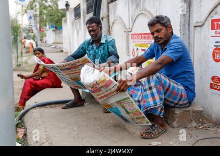 Due uomini che leggono il giornale su un marciapiede a Trichy, Tamil Nadu, India Foto Stock