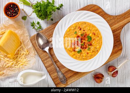 zuppa di mais con pancetta fritta croccante sbriciolata in ciotola bianca su tavola bianca in legno testurizzato con ingredienti, vista orizzontale dall'alto, piatta Foto Stock