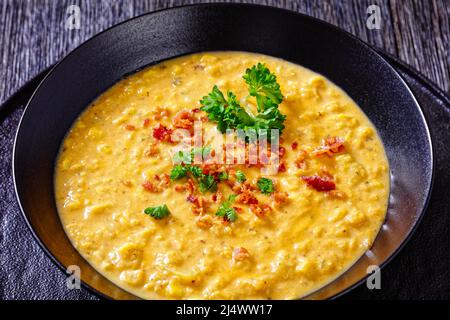 zuppa di mais con pancetta fritta croccante sbriciolata in una ciotola nera su un tavolo di legno scuro, vista orizzontale dall'alto, primo piano Foto Stock