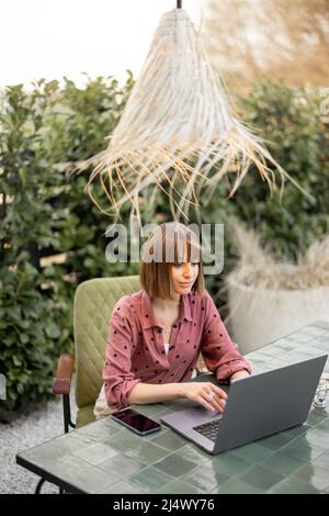 La donna lavora su un notebook online in giardino all'aperto Foto Stock
