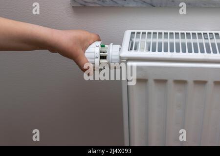 Vista ravvicinata della mano del bambino spegnimento del termostato sul radiatore di riscaldamento per risparmiare energia. Svezia. Foto Stock
