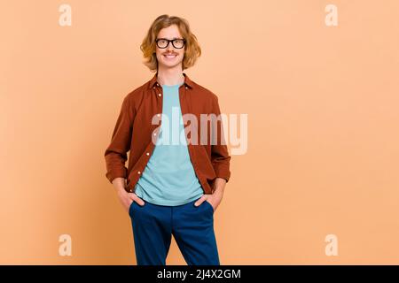 Ritratto di attraente allegro ragazzo rosso-capelli tenendo le mani in tasche isolato su sfondo beige color pastello Foto Stock