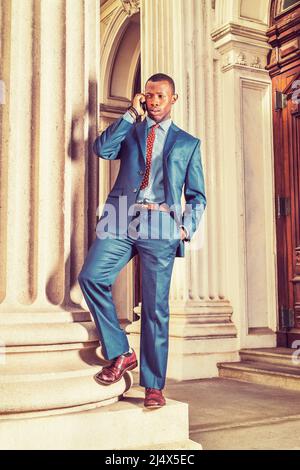 Vestito in abito blu, cravatta, scarpe in pelle, borsone auricolare,  bracciale, un giovane uomo d'affari nero che si erge fuori da un edificio  d'ufficio in stile vintage, frown, unhappp Foto stock -