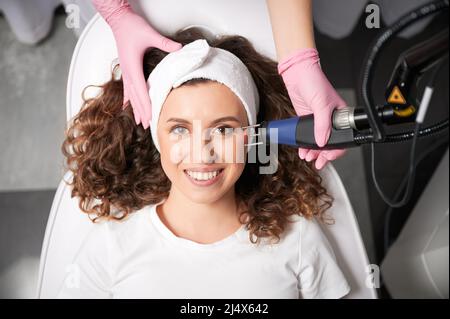 Primo piano ritratto di ragazza curly con vecchio post acne che rimuovendo da laser faccia lucidare. Il processo di fototermolisi, scaldando la pelle in cosmetologia hardware per la pulizia della pelle. Foto Stock