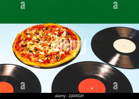 Cibo pop arte fotografia. Pizza italiana adagiata su dischi di vinile su tovaglia leggera isolata su sfondo verde. Vintage, moda retrò, musica Foto Stock