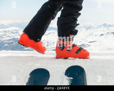 Sciatore in scarponi da sci rosso che cammina sul bordo della montagna con la cima ovale dello sci e grande cresta di montagna in lontananza Foto Stock