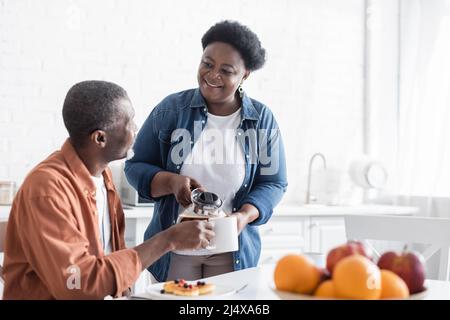 happy african american moglie che serve caffè a sorridere marito durante la colazione Foto Stock