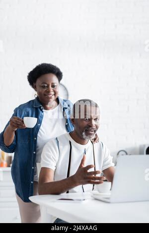 shocked uomo afroamericano gesturing vicino moglie mentre guarda il laptop Foto Stock