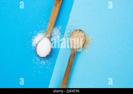 cristalli di zucchero bianco e marrone su cucchiai di tè in legno e sfondo blu Foto Stock