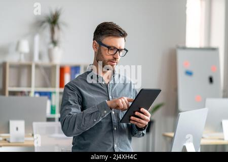 Tecnologie moderne nel business. Concentrato uomo d'affari maturo che utilizza tablet digitali in ufficio Foto Stock