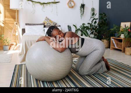 Giovane donna incinta che si appoggia sulla palla fitness durante le contrazioni che soffrono di dolore Foto Stock