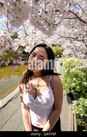 Giovane donna indossa abiti casual circondati da fiori di ciliegio Foto Stock