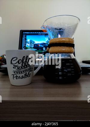 Wroclaw, Polonia - Aprile 2021: Caraffa di caffè Chemex piena di caffè e tazza bianca davanti al computer portatile Foto Stock