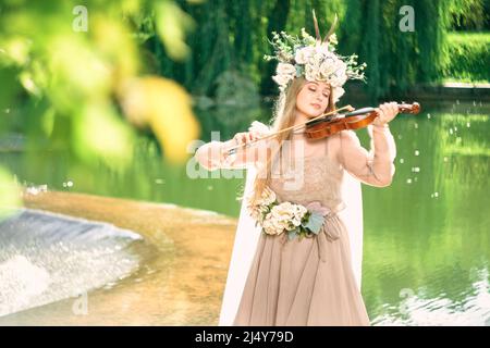 ragazza in un abito suona il violino vicino ad una cascata Foto Stock