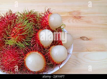 Piatto di Rambutan fresco sbucciato maturo con frutta intera su tavola di legno Foto Stock